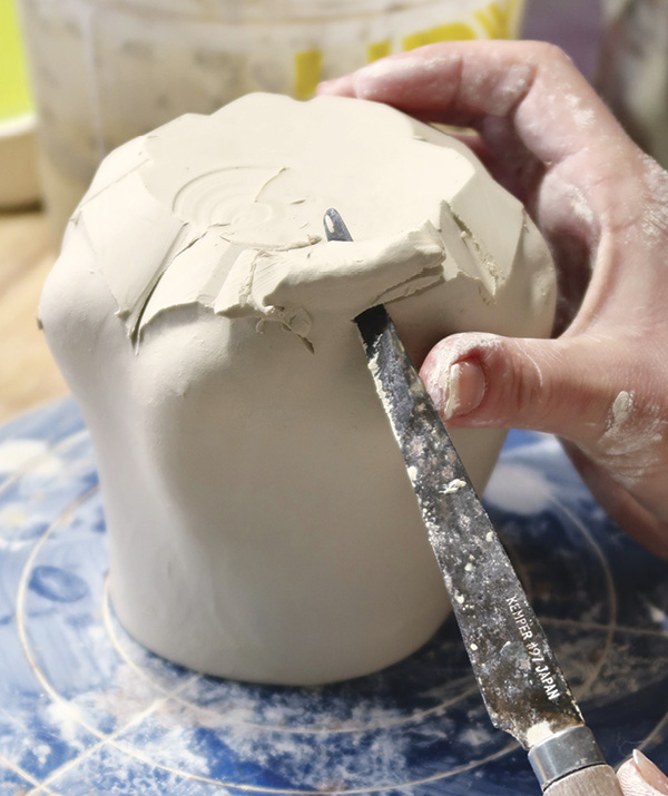 6 Using a fettling knife, cut excess clay away from the perimeter of the foot, following the curves around the mug.